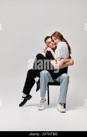 Ein junger Mann und eine junge Frau sitzen ineinander auf einem Stuhl, ihre Blicke sind in einem Moment der gemeinsamen Verbindung und Liebe eingeschlossen. Stockfoto