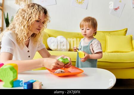 Eine lockige Mutter spielt in einem gemütlichen Wohnzimmer mit ihrer Tochter Montessori und fördert das Lernen und Binden. Stockfoto