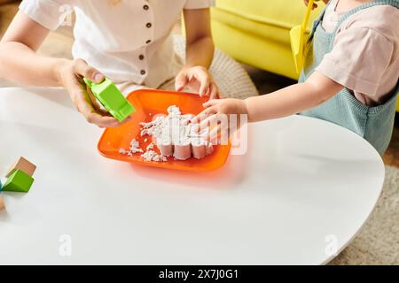 Zwei Kinder, ein Kleinkind mit lockigen Haaren und ein älteres Kind, spielen mit Spielzeug auf einem Tisch, indem sie die Montessori-Erziehungsmethode anwenden. Stockfoto