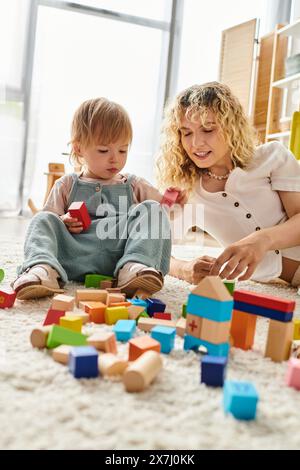 Eine lockige Mutter und ihre Kleinkind-Tochter verbinden sich und lernen durch Spiel mit Blöcken auf dem Boden zu Hause. Stockfoto