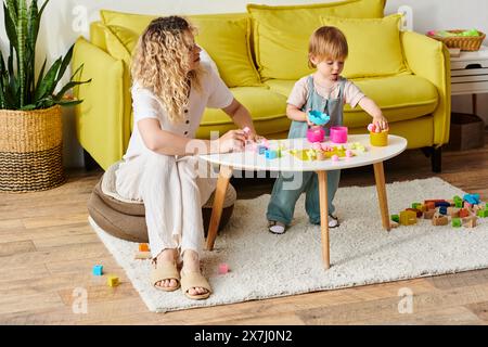 Eine Mutter mit lockigen Haaren, die ihre Tochter in Montessori anzieht, spielt und lernt in einem gemütlichen Wohnzimmer. Stockfoto