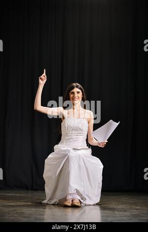 Elegante Frau in weißem Kleid sitzt anmutig auf der Bühne während der Proben. Stockfoto