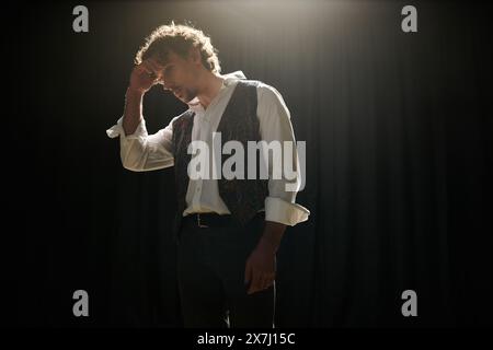 Ein Mann in Weste und Krawatte steht selbstbewusst in einem schwach beleuchteten Raum. Stockfoto