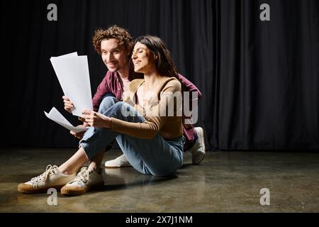 Mann und Frau sitzen auf dem Boden, halten Papiere und diskutieren das Theaterskript. Stockfoto