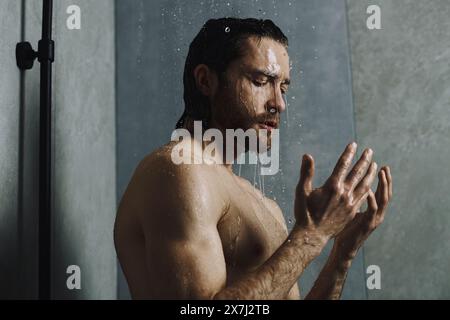 Ein Mann, der unter der Dusche steht, seine Hände in der Luft hält und seine morgendliche Routine genießt. Stockfoto