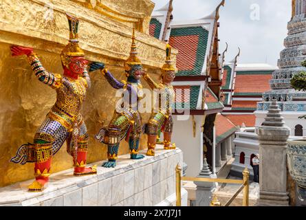 Ein Bild von Statuen am Fuße eines goldenen Chedi im Großen Palast in Bangkok. Stockfoto