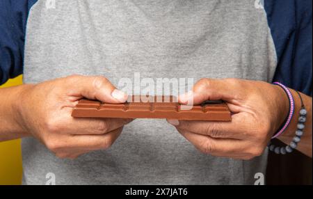 Hände eines nicht erkennbaren Mannes, der eine Schokoladenriegel bricht, um sie zu konsumieren Stockfoto