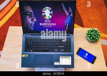 Hintergrundbild der UEFA-Fußball-Europameisterschaft 2024 auf einem Laptop-Bildschirm und Logo der UEFA-Fußball-Europameisterschaft 2024 auf einem Telefonbildschirm, Draufsicht Stockfoto