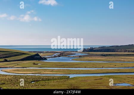 Ein Blick über das Cuckmere Valley mit dem Fluss, der sich zum Meer hin windet, und einem blauen Himmel über Ihnen Stockfoto