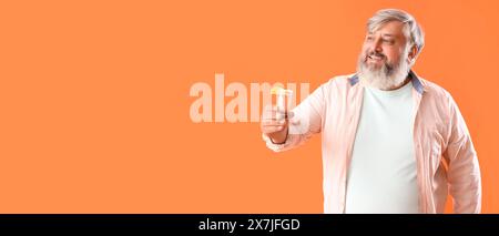 Porträt eines Reifen bärtigen Mannes, der einen Tequila-Schuss auf orangem Hintergrund mit Platz für Text hält Stockfoto