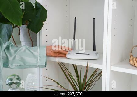 Frau mit wlan-Router im Regal zu Hause, Nahaufnahme Stockfoto