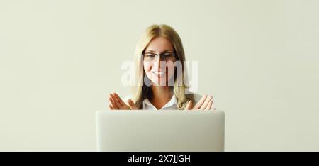 Glückliche junge Frau, die an Laptop-Begrüßungen arbeitet, kommuniziert mit Freunden per Videoanruf, die am Schreibtisch im Büro oder zu Hause sitzt Stockfoto