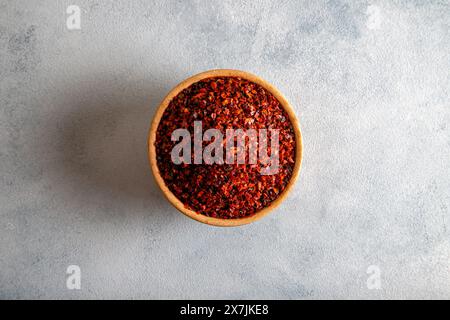 Rote Pfefferflocken. Rote Chilischoten in Holzschale auf hellblauem Hintergrund Stockfoto