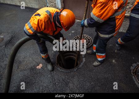 Kanalisationsarbeiter, die den Gullyschacht reinigen und die Kanalisation auf der Straße freimachen. Stockfoto