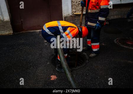 Kanalisationsarbeiter, die den Gullyschacht reinigen und die Kanalisation auf der Straße freimachen. Stockfoto