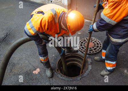 Kanalisationsarbeiter, die den Gullyschacht reinigen und die Kanalisation auf der Straße freimachen. Stockfoto