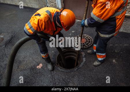 Kanalisationsarbeiter, die den Gullyschacht reinigen und die Kanalisation auf der Straße freimachen. Stockfoto