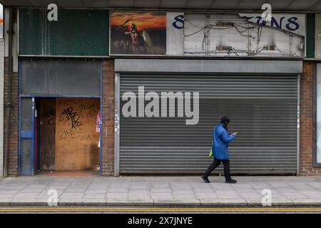 Eine Frau, die an einem geschlossenen Laden vorbeiläuft, High Street, Strood, Kent, Großbritannien. April 2024 Stockfoto