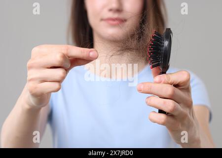 Frau, die ihr verlorenes Haar von der Bürste auf grauem Hintergrund nimmt, Nahaufnahme. Alopezie-Problem Stockfoto