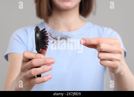 Frau, die ihr verlorenes Haar von der Bürste auf grauem Hintergrund nimmt, Nahaufnahme. Alopezie-Problem Stockfoto