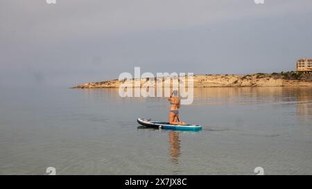 Mai 2024: Junge Frau paddelt in einem ruhigen Meer in der Coral Bay bei Pafos, Zypern. Stockfoto