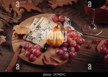 Käseplatte mit Rotwein, Herbstfrüchten und trockenen Blättern Stockfoto
