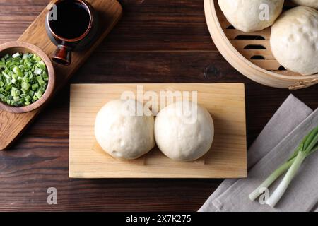 Köstliche chinesische gedämpfte Brötchen, grüne Zwiebeln und Sojasauce auf Holztisch, flache Ladefläche Stockfoto