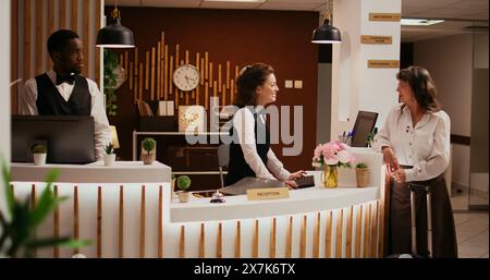 Ältere Person, die in der Hotellobby ankommt und den Concierge nach Angeboten für Seniorenreisen für Wellness und Freizeitaktivitäten fragt. Mitarbeiter begrüßt Touristen an der Rezeption und sorgt für einen erholsamen Aufenthalt. Stockfoto