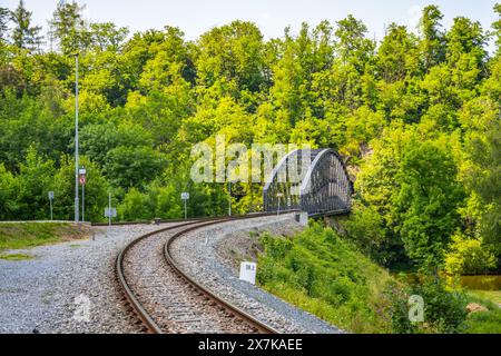 Eine gekrümmte Eisenbahnbrücke in Rataje, umgeben von dichtem Grün und Bäumen im Sommer, mit Eisenbahngleisen, die zur Brücke führen. Stockfoto