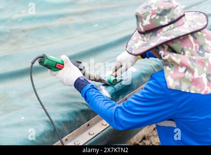 Heißkeilgebläse, das Kunststoffleinen und Rollenkompresse auf der Abwasserkuppel aufsetzt. Stockfoto