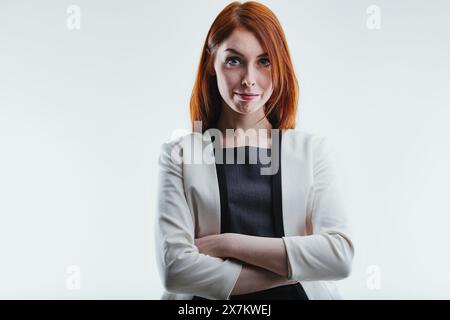 Professionell aussehende Frau mit leuchtend roten Haaren und verspieltem Grinsen, gekleidet in einem stylischen grauen Blazer, strahlt Selbstvertrauen aus Stockfoto