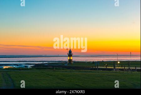 Der schwarz-weiße Leuchtturm, die kleine Preusse genannt, steht kurz nach Sonnenuntergang an der Nordsee unter einem bunten Himmel Stockfoto