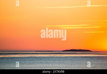 Himmel und Meer bei einem malerischen, goldenen, atemberaubend schönen Sonnenuntergang über dem Meer, Insel Langluetjen II am Horizont, orange leuchtend wolkenlos Stockfoto