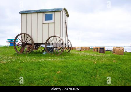 Alter Holzwagen, Badewagen mit Zugstange und großen Holzrädern auf einer grünen Wiese, im Hintergrund viele Liegen, bewölkter Tag, einsam, Meer Stockfoto