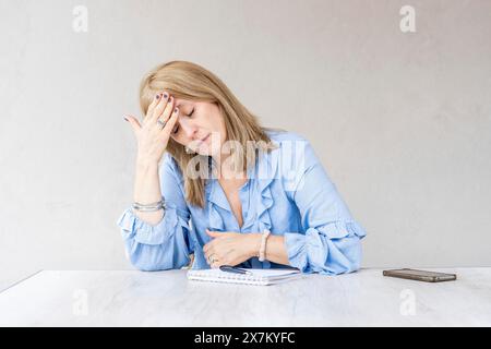 Eine mittelerwachsene blonde Frau hält eine Hand auf der Stirn Stockfoto