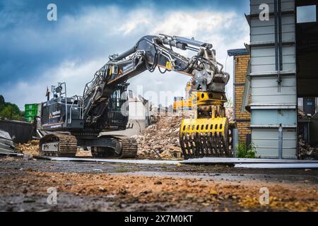 Ein Bagger mit schwerem Gerät arbeitet auf einer Baustelle, der Himmel ist bewölkt und die Umgebung ist voller Schutt, Abbruch Stockfoto