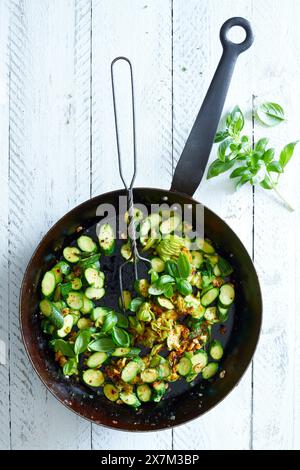 Gebratene Zucchini-Blüten mit Basilikum, in einer schwarzen Pfanne, auf weißem hölzernem Hintergrund Stockfoto