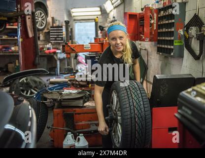 Ein Mädchen, das in einer Garage einen Autoreifen wechselt. Stockfoto