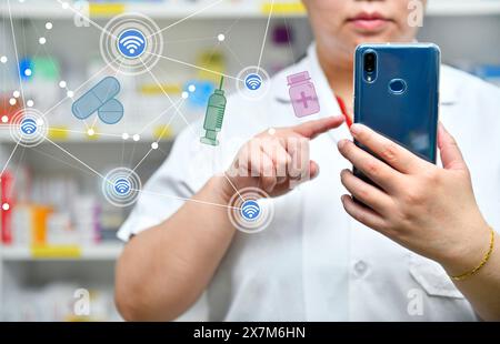 Ein Apotheker hält ein Mobiltelefon, um ein ärztliches Rezept zu erhalten, Medikamente zuzubereiten und Medikamente in einer Apotheke zu überprüfen. Stockfoto