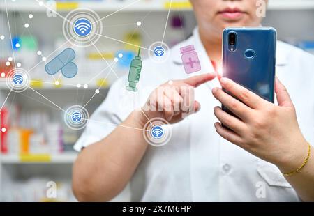 Ein Apotheker hält ein Mobiltelefon, um ein ärztliches Rezept zu erhalten, Medikamente zuzubereiten und Medikamente in einer Apotheke zu überprüfen. Stockfoto