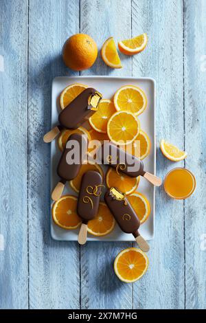 Schokoladen-Orange-Eis auf einer weißen Platte mit frisch geschnittenen Orangenscheiben auf blauem Holzhintergrund Stockfoto