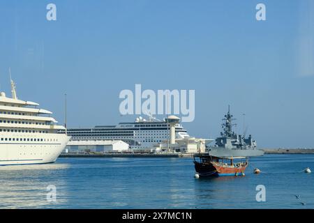 Muscat, Oman - 2. Januar 2024: Ein ruhiger Blick auf den Hafen mit einem traditionellen omanischen Boot im Vordergrund mit modernen Kreuzfahrtschiffen und einer Marine Stockfoto