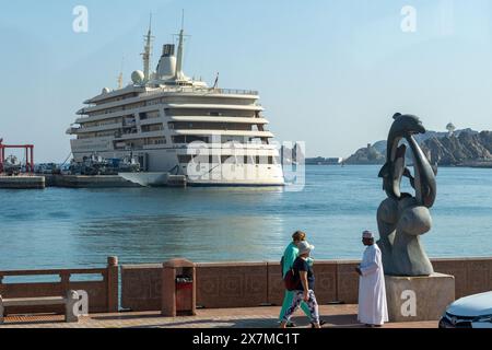 Muscat, Oman - 2. Januar 2024: Ein Einheimischer in traditioneller Kleidung und ein Tourist in westlicher Kleidung spazieren an einer modernen Kunstskulptur am Meer vorbei Stockfoto