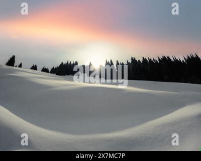 Sonnenaufgang in den Winterbergen Zentralasiens. Die Morgensonne blickt hinter dem Berg hervor und beleuchtet den schneebedeckten Hang Stockfoto
