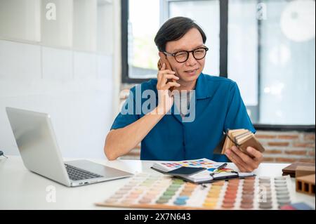 Ein erfahrener asiatischer Innenarchitekt oder -Designer spricht mit seinem Kunden, während er im Büro arbeitet. Bauunternehmen Stockfoto