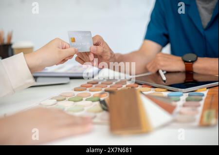 Ein Nahbild einer Kundin, die während der Besprechung im Büro ihre Kreditkarte ihrem Auftragnehmer oder Innenarchitekten übergibt. Unternehmer Stockfoto