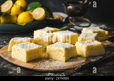 Seitenwinkel der quadratischen Zitronenkuchenscheiben, belegt mit Puderzucker, mit frischer Zitrone im Hintergrund Stockfoto