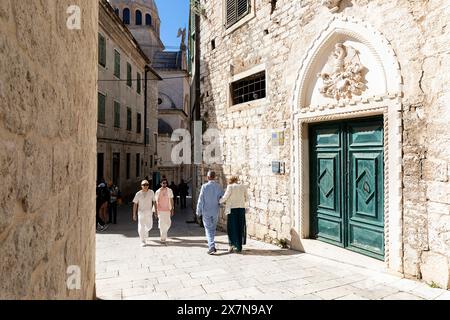 Touristen gehen zu Fuß, erkunden wunderschöne alte traditionelle Gebäude, Häuser aus Stein in der historischen Altstadt von Sibenik in Dalmatien, Kroatien Stockfoto