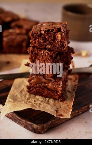 Brownie-Scheiben auf Holzbrett gestapelt mit Messer und Teetasse Stockfoto