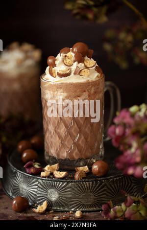 Ein Glasbecher mit gemalzter heißer Schokolade, garniert mit Creme- und Chocolate-Malzbällchen. Stockfoto